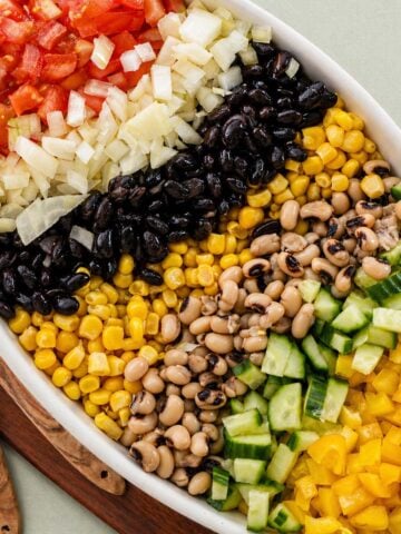 cowboy caviar with black beans corn black eyed peas cucumber tomatoes and onion arranged in a bowl