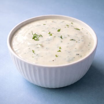 Creamy dill sauce for salmon served in a white bowl on a soft blue background
