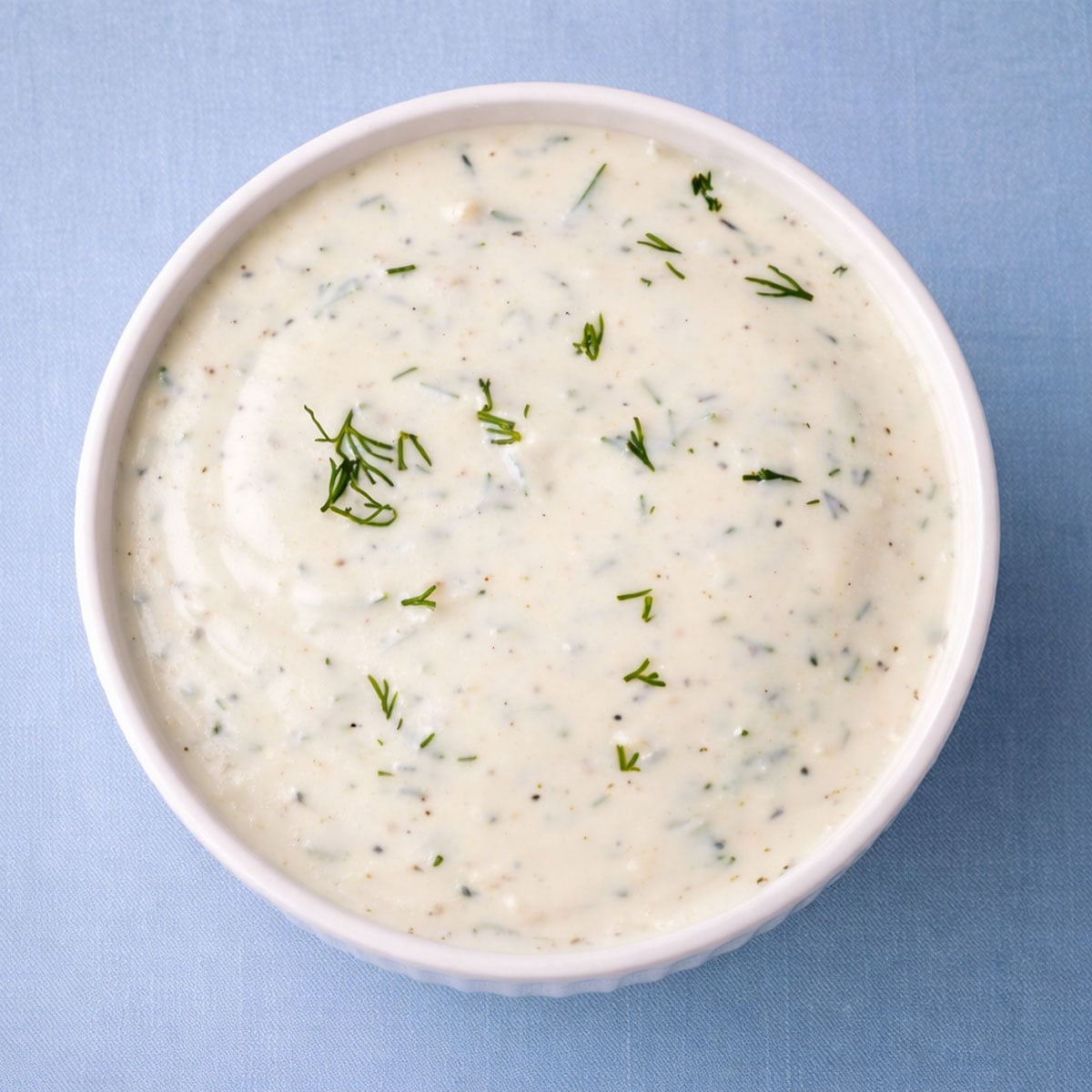 Top-down view of creamy dill sauce for salmon in a white bowl on a soft blue background