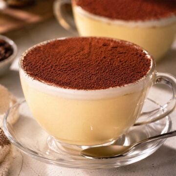 Creamy flan with heavy cream served in glass cups, topped with cocoa powder and presented as an elegant individual custard dessert.