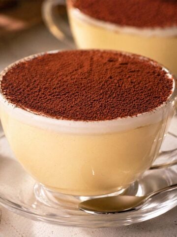 Creamy flan with heavy cream served in glass cups, topped with cocoa powder and presented as an elegant individual custard dessert.