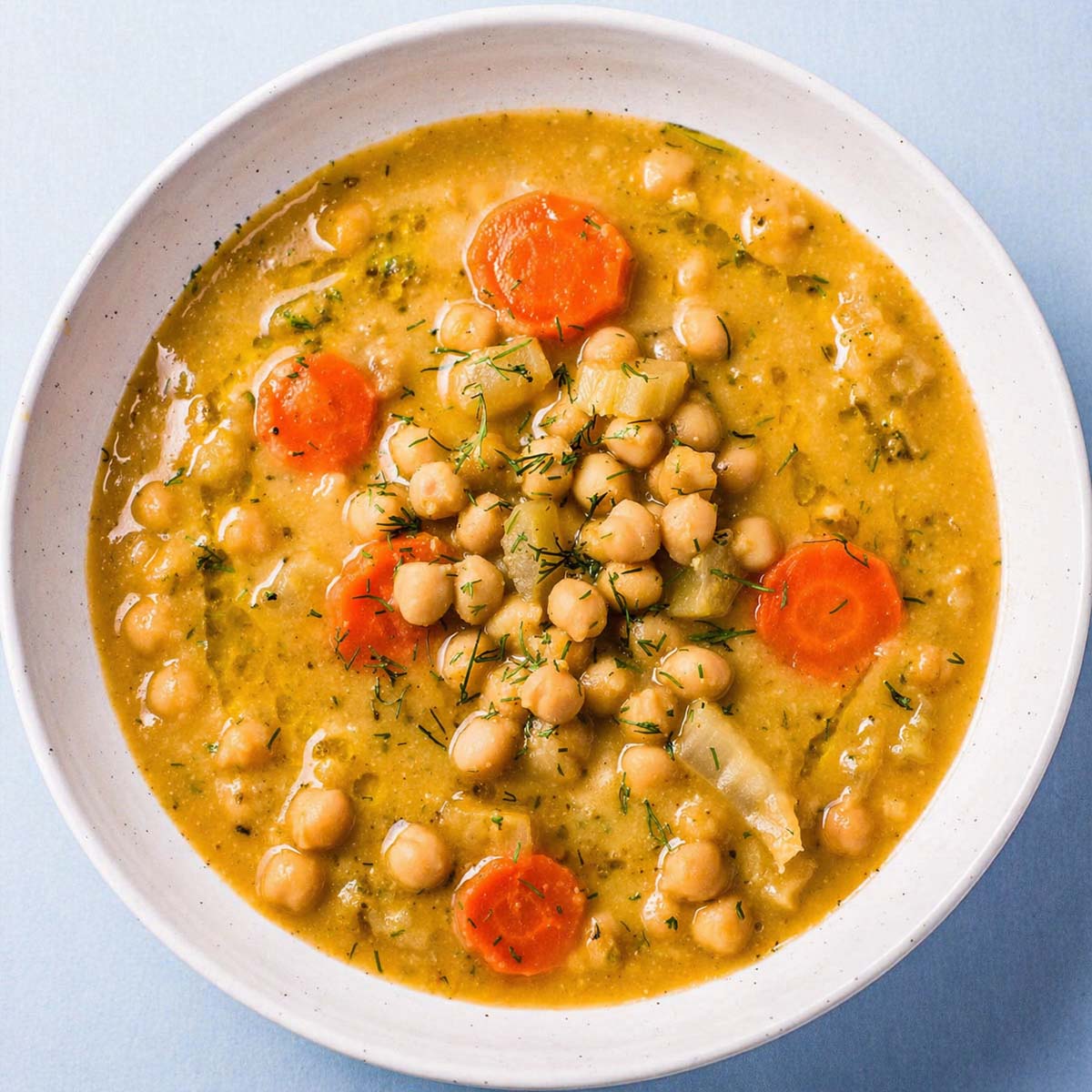 creamy lemon chickpea soup with carrots and herbs in a white bowl, Mediterranean chickpea soup top view