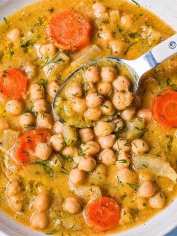 creamy lemon chickpea soup with carrots and herbs, spoon lifting chickpeas from a bowl of Mediterranean chickpea soup