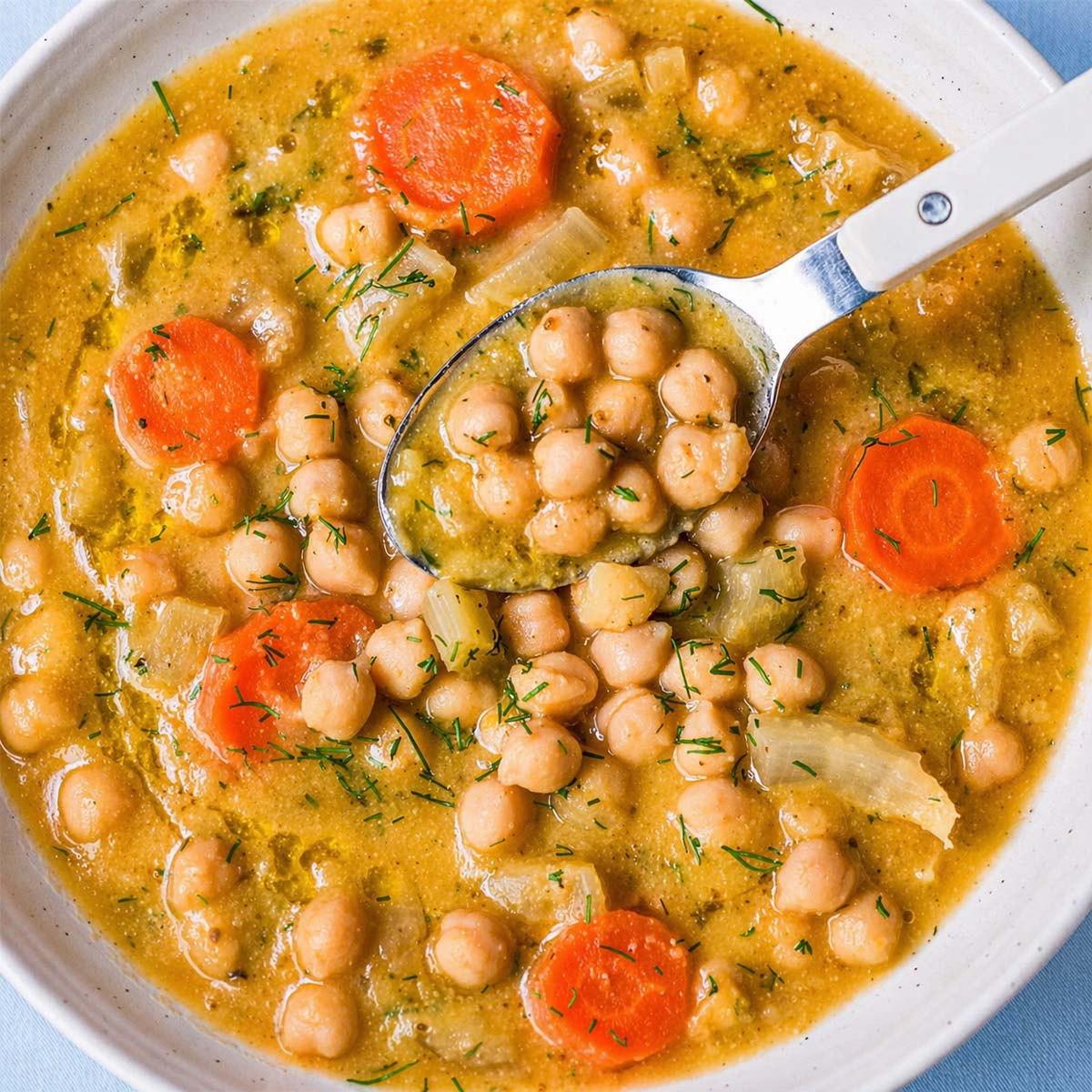 creamy lemon chickpea soup with carrots and herbs, spoon lifting chickpeas from a bowl of Mediterranean chickpea soup