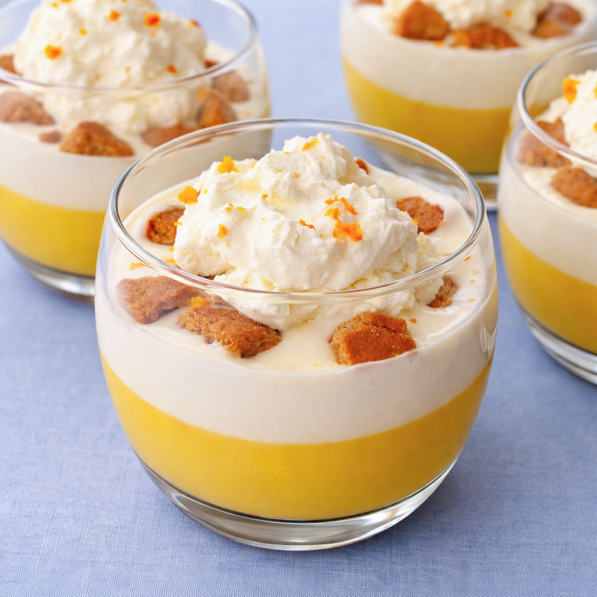 Creamy orange pudding dessert in a glass cup with layers of citrus pudding, vanilla cream, biscuit pieces, and whipped cream topped with orange zest.