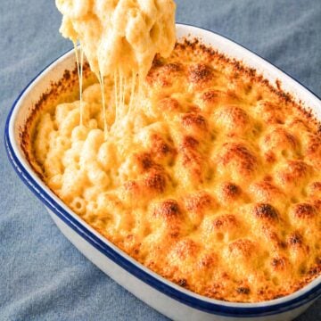easy baked mac and cheese in a white casserole dish with golden bubbly cheese crust and creamy macaroni being lifted with melted cheese strings