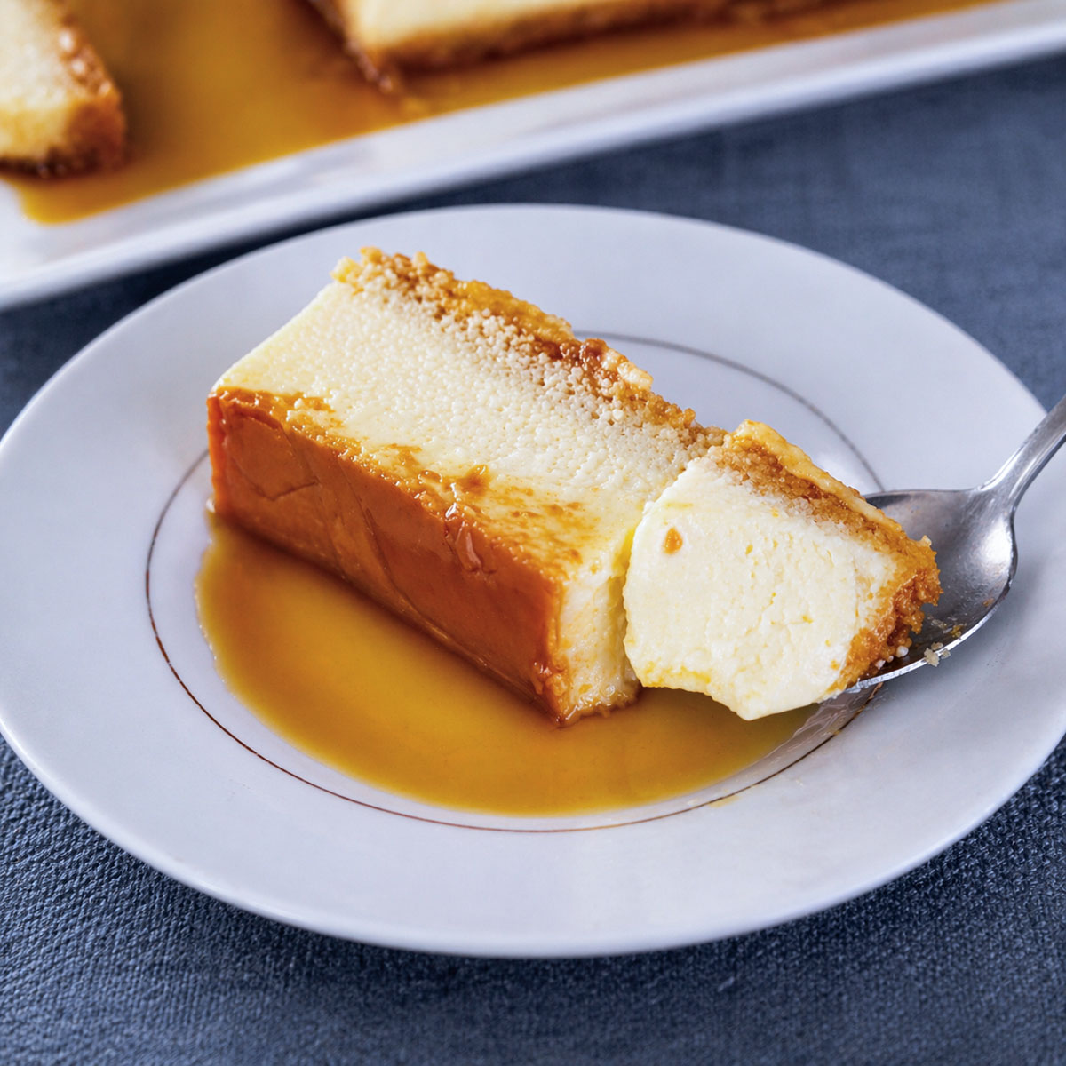 easy flan recipe without condensed milk with creamy custard bite on spoon and caramel sauce on white plate