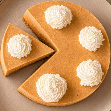 Easy No Bake Pumpkin Cheesecake topped with whipped cream rosettes, sliced and served on a plate
