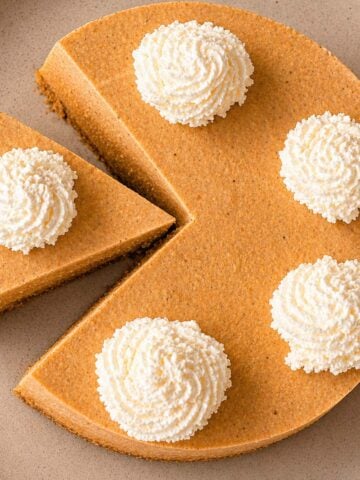 Easy No Bake Pumpkin Cheesecake topped with whipped cream rosettes, sliced and served on a plate