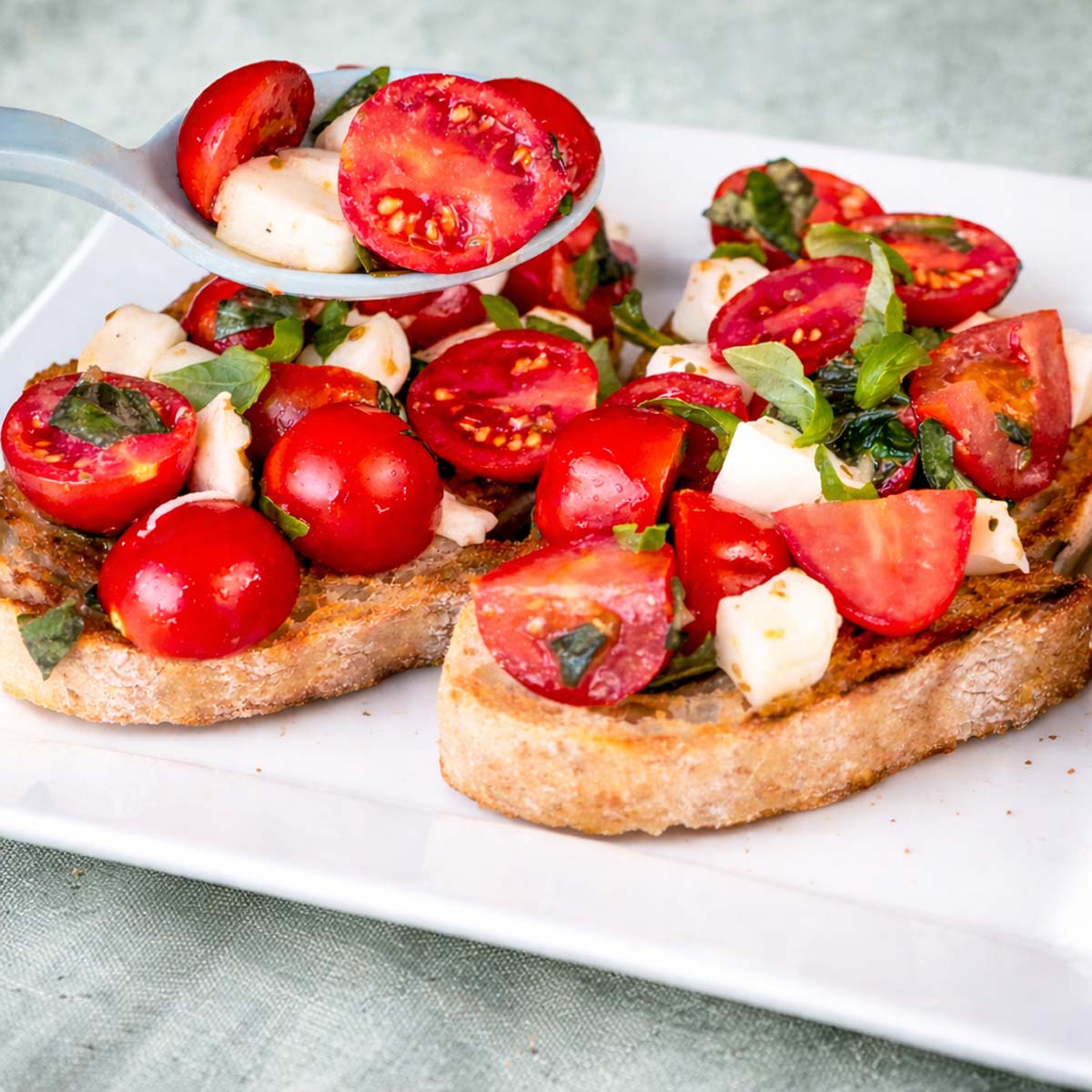 Cherry tomato bruschetta with mozzarella, basil, and olive oil served on toasted bread slices.