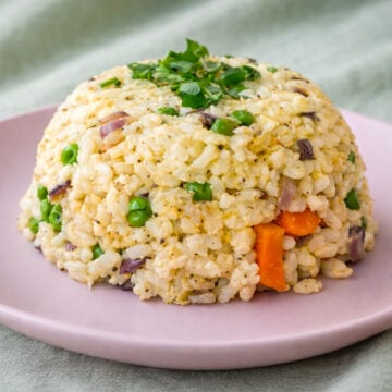 Egg fried rice with peas, carrots, and red onion served on a pink plate, topped with fresh parsley.