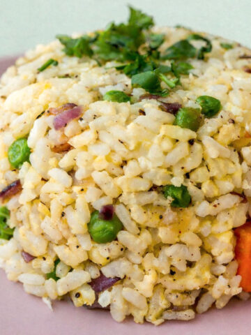 Egg fried rice with peas, carrots, red onion, and scrambled egg served on a pink plate, topped with fresh parsley.