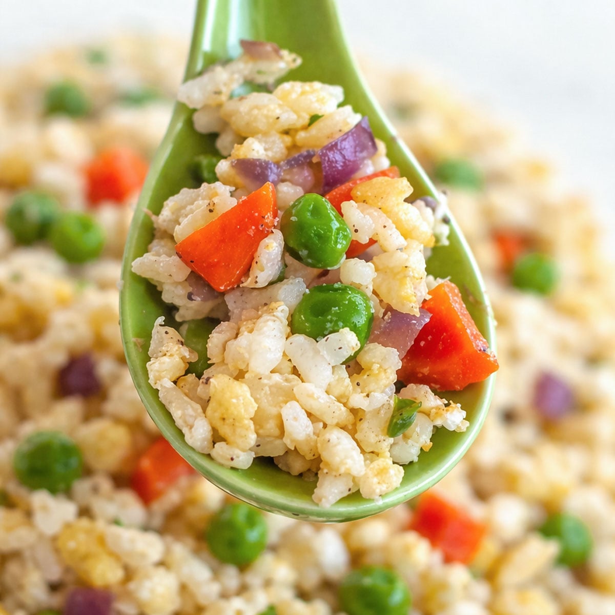 Spoonful of Easy Vegetable Egg Fried Rice  with peas, carrots, red onion, and scrambled egg above a plate of fried rice.