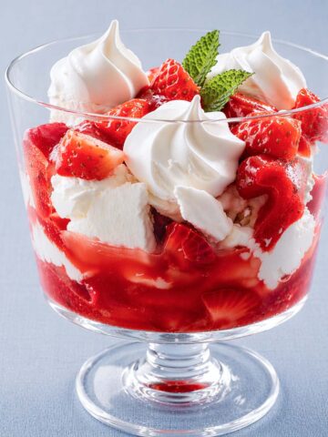 Eton mess dessert in a glass coupe with strawberries, whipped cream, meringue, and min