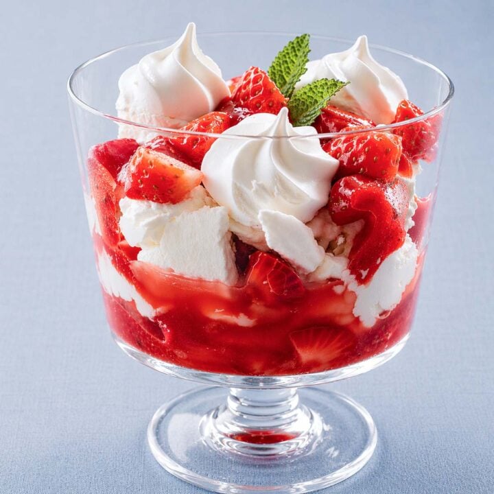 Eton mess dessert in a glass coupe with strawberries, whipped cream, meringue, and min