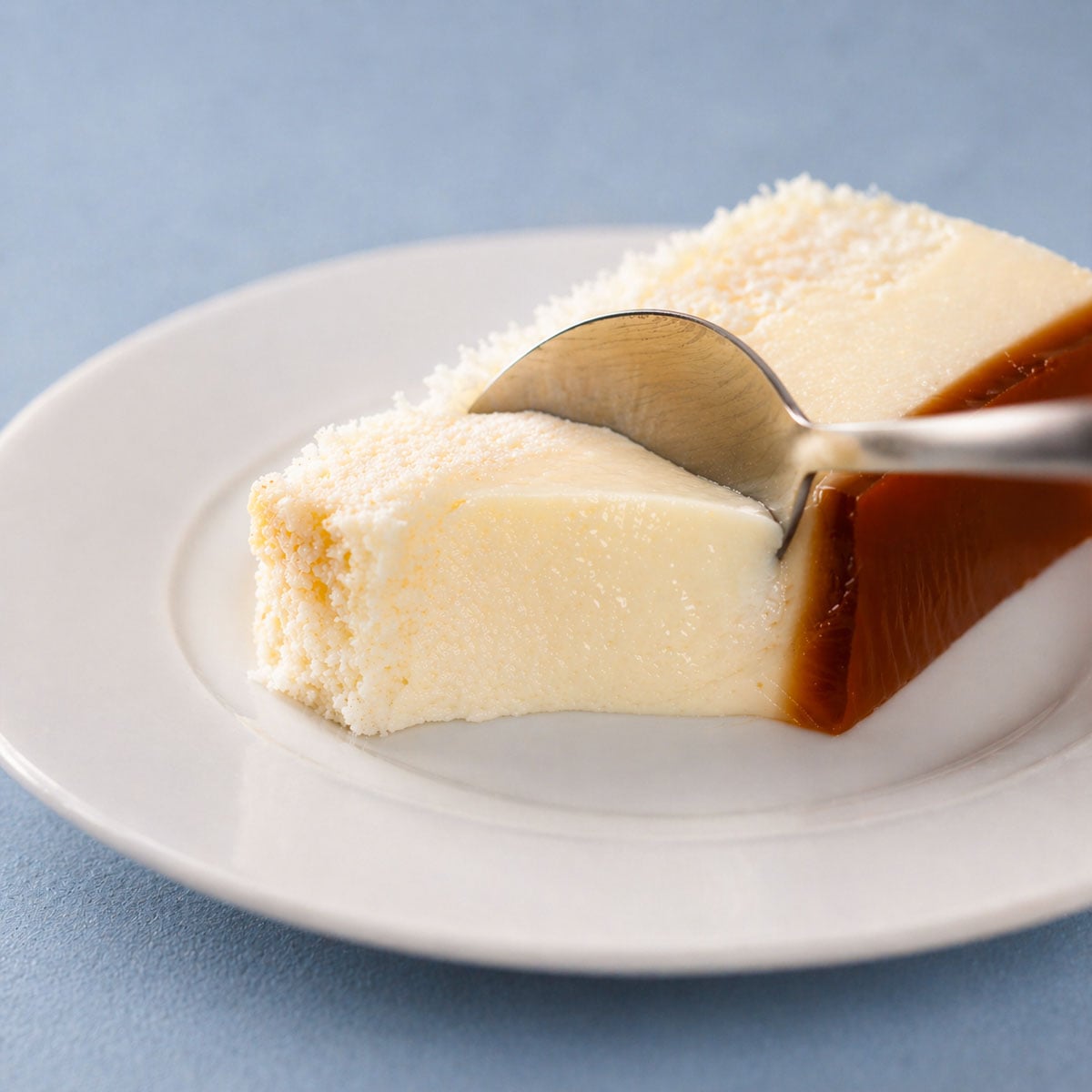 flan cake slice with creamy texture and caramel layer being scooped with spoon on white plate