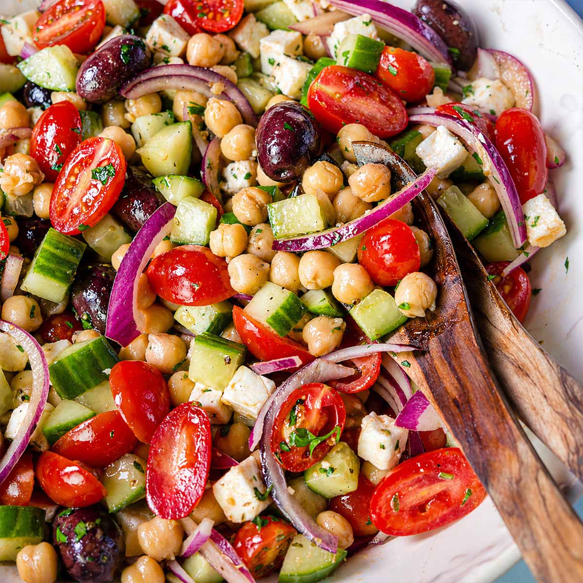 Close up Greek chickpea salad with feta, cucumber, cherry tomatoes, red onion, and olives in a bowl