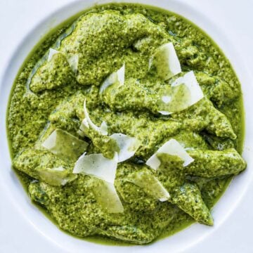 Homemade pesto pasta topped with shaved Parmesan cheese in a white bowl, close-up overhead view