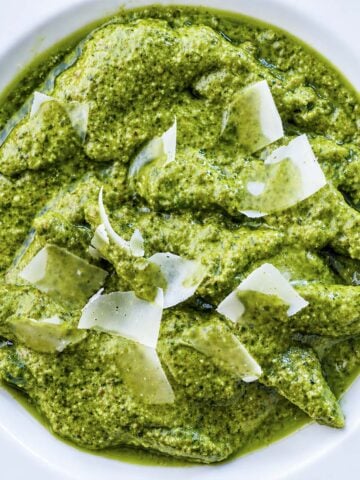 Homemade pesto pasta topped with shaved Parmesan cheese in a white bowl, close-up overhead view