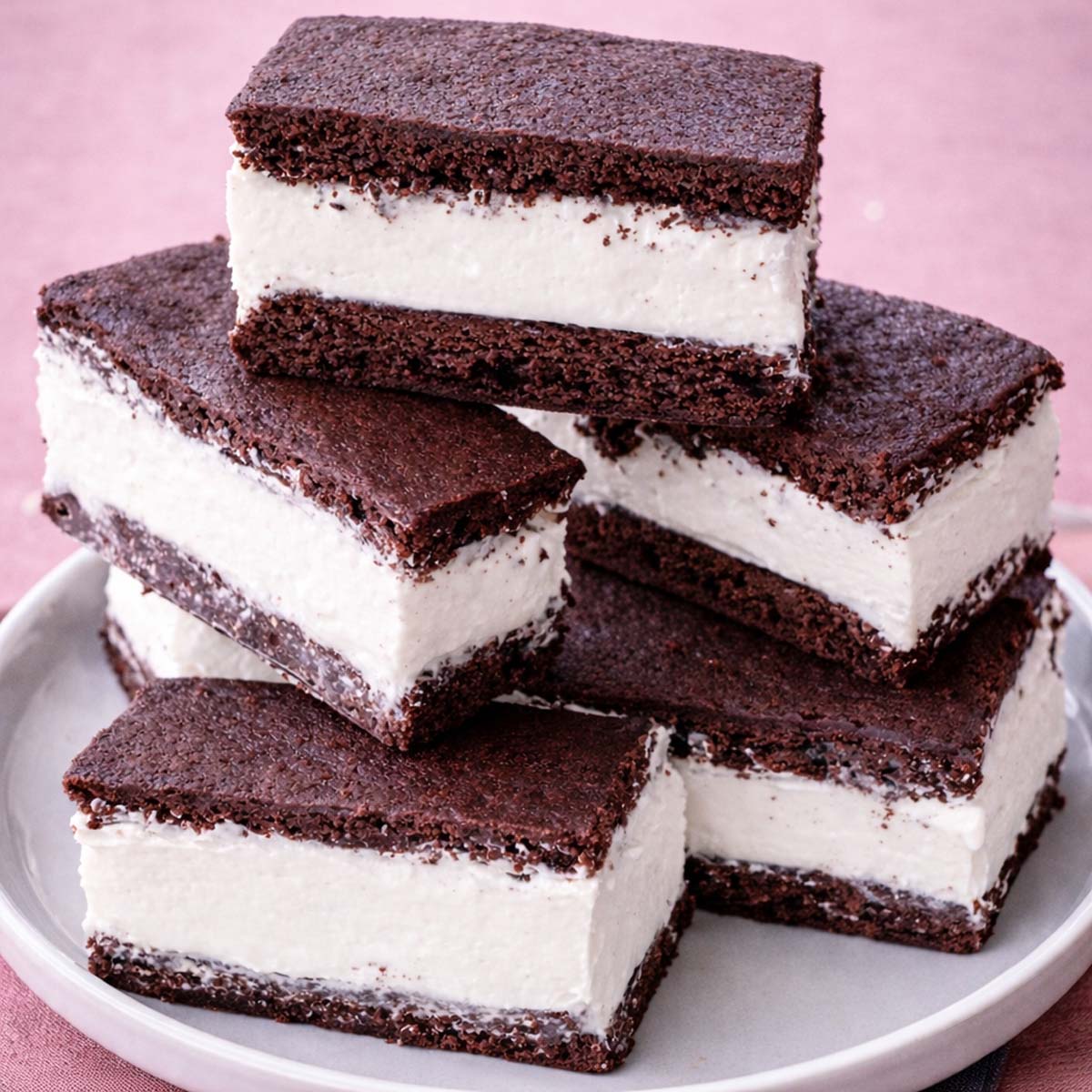 Homemade Vanilla Ice Cream Sandwiches with Brownies stacked on a white plate, showing thick creamy vanilla ice cream between soft chocolate brownie layers.