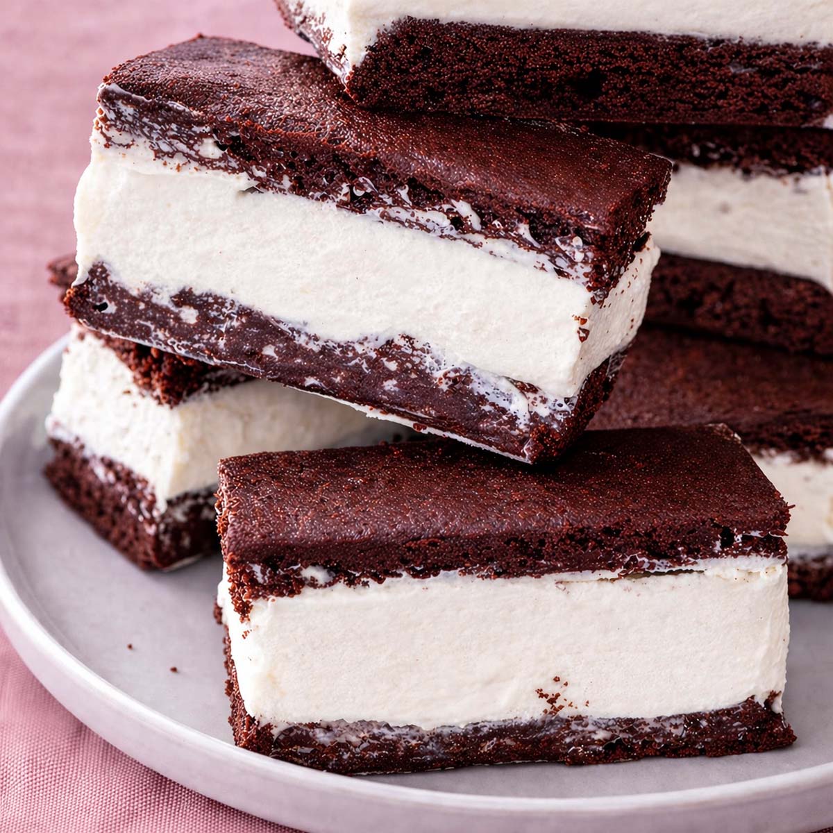 Homemade Vanilla Ice Cream Sandwiches with Brownies stacked on a white plate, featuring thick vanilla ice cream layered between soft chocolate brownie squares.