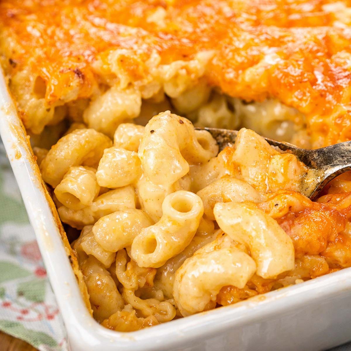 Homemade baked mac and cheese with creamy elbow pasta and golden melted cheddar topping in a baking dish being served with a spoon