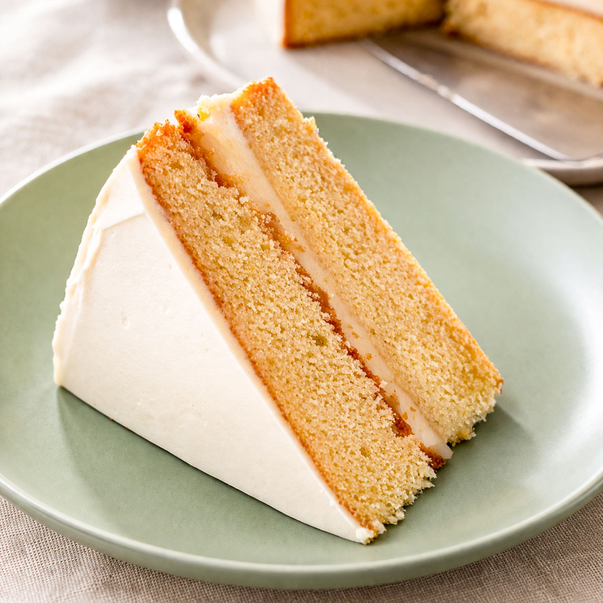 Slice of lemon curd layer cake with cream cheese frosting showing moist lemon sponge and lemon curd filling on a plate.