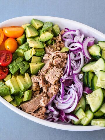 Mediterranean tuna salad with avocado, cucumber, cherry tomatoes, and red onion in a white bowl