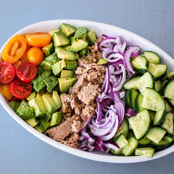 Mediterranean tuna salad with avocado, cucumber, cherry tomatoes, and red onion in a white bowl