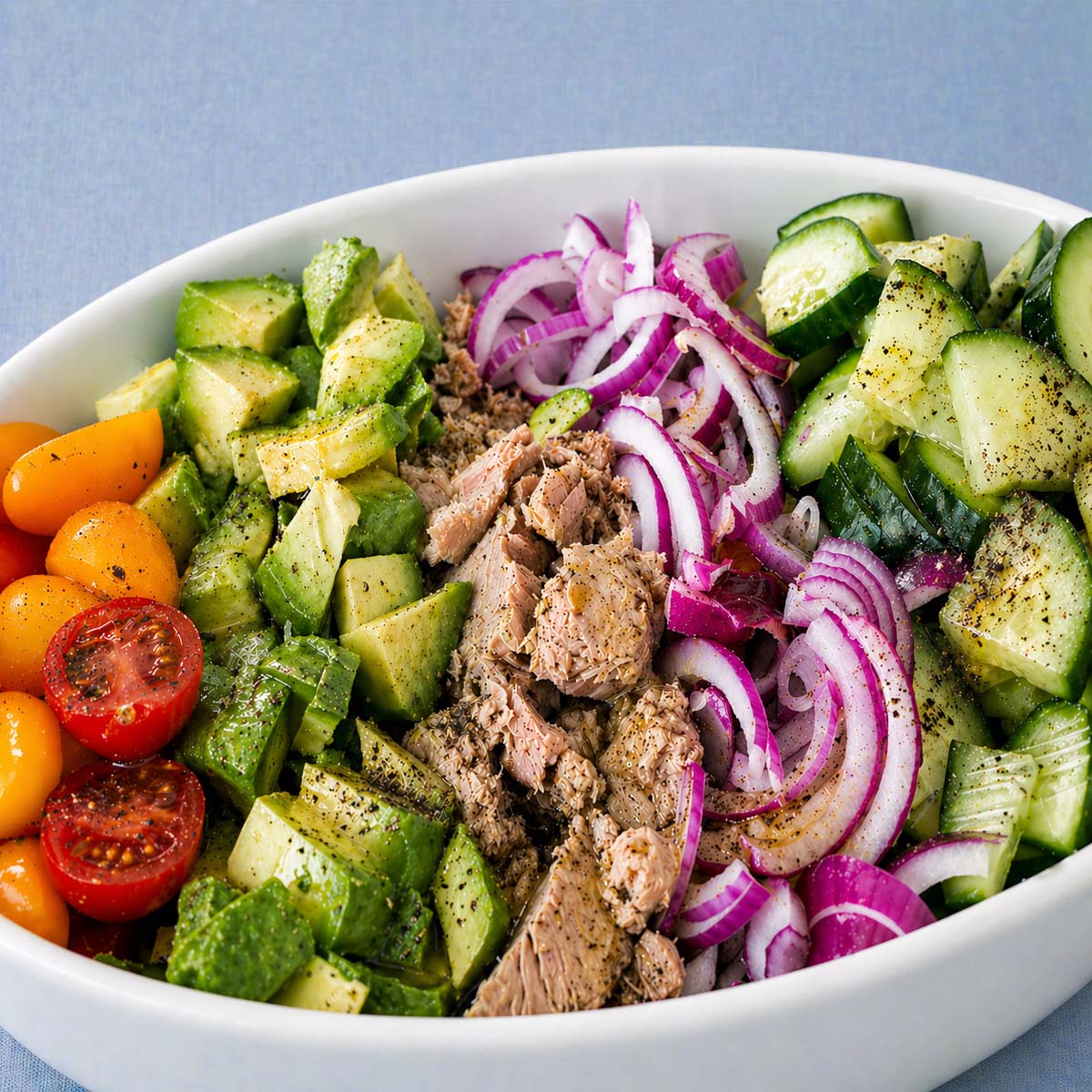 Closeup Mediterranean tuna salad with avocado, cucumber, cherry tomatoes, and red onion in a white bowl
