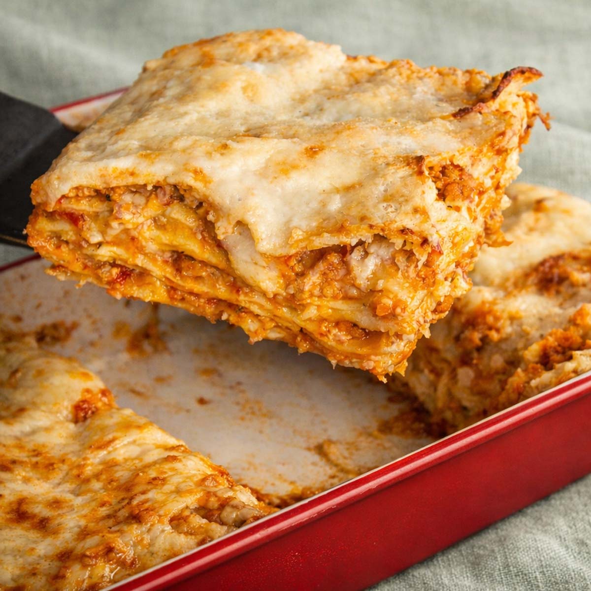 Slice of easy no-boil lasagna with pork Bolognese, béchamel sauce, and melted cheese in a baking dish 