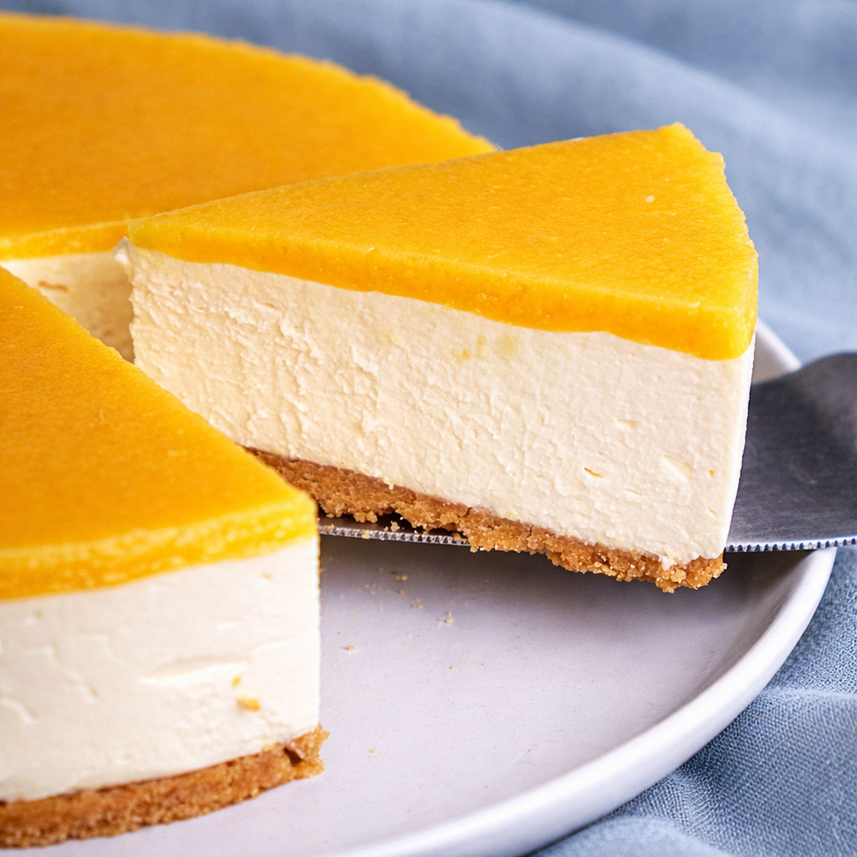 Slice of No-Bake Orange Creamsicle Cheesecake with a glossy orange topping and biscuit crust lifted onto a plate.