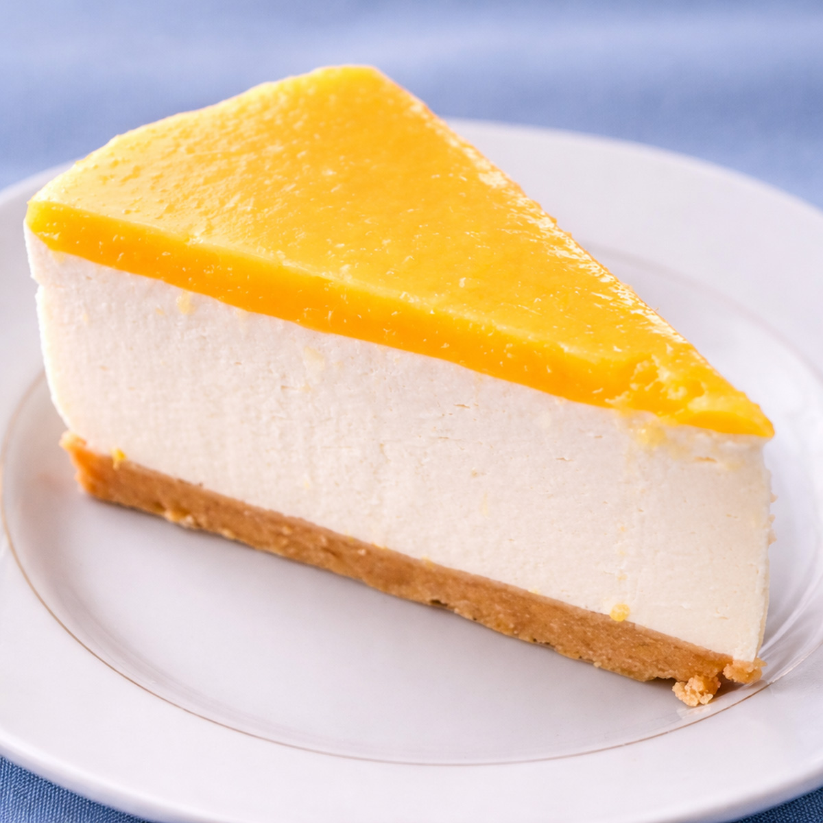 Slice of no-bake orange creamsicle cheesecake with a smooth orange topping, creamy cheesecake layer, and biscuit crust on a white plate. 