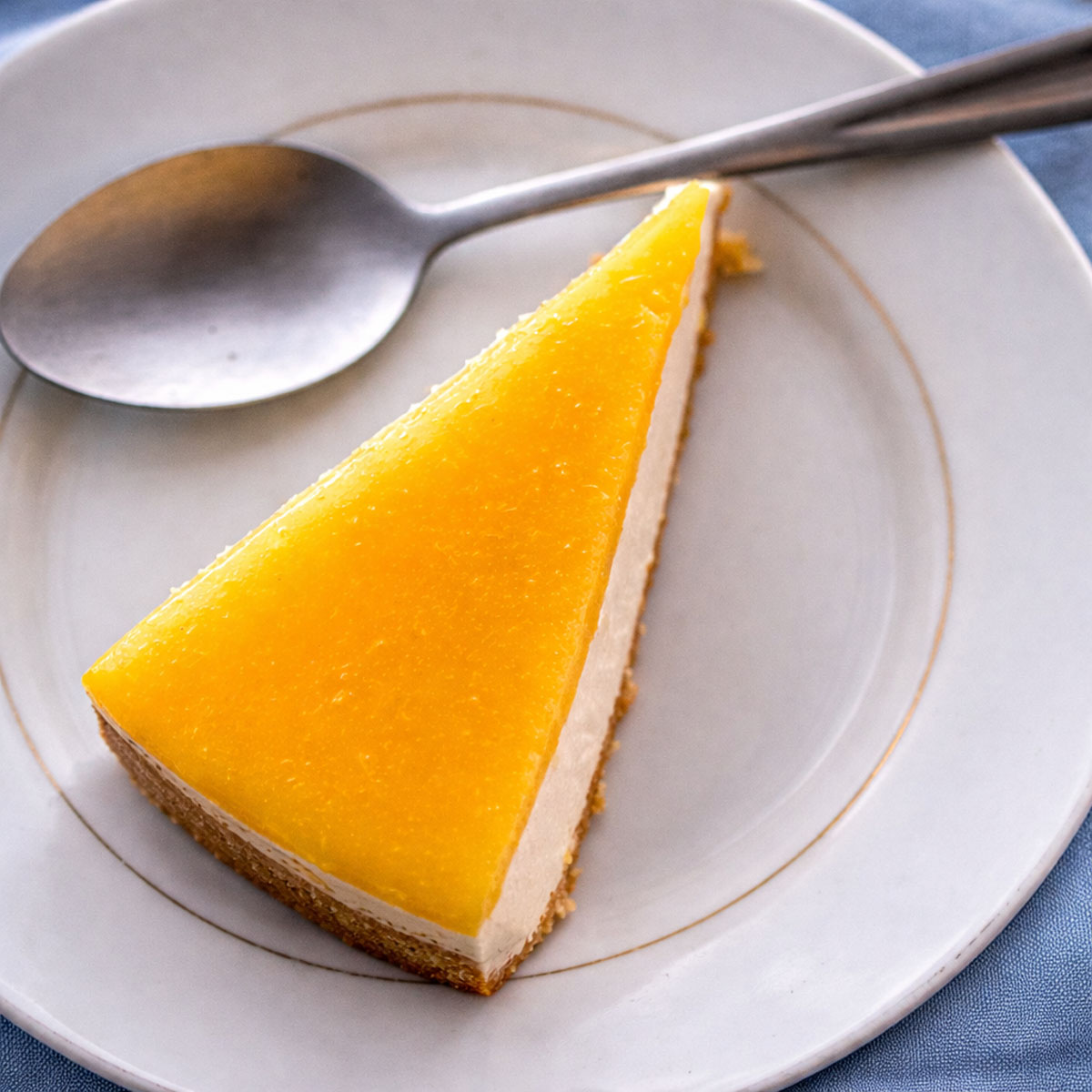Top-down view of a slice of No-Bake Orange Creamsicle Cheesecake with glossy orange topping on a white plate, with a spoon beside it. 