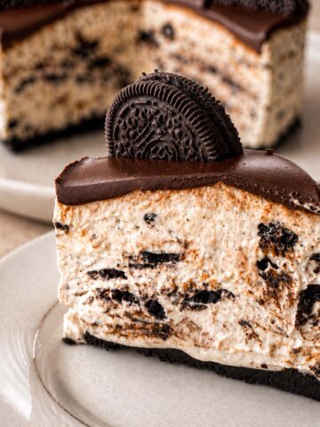 no-bake Oreo cheesecake slice with chocolate ganache on a plate, creamy cookies and cream filling and Oreo crust