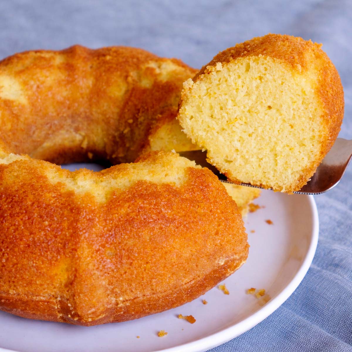 orange juice cake bundt with slice lifted on a cake server showing soft moist crumb on a white plate
