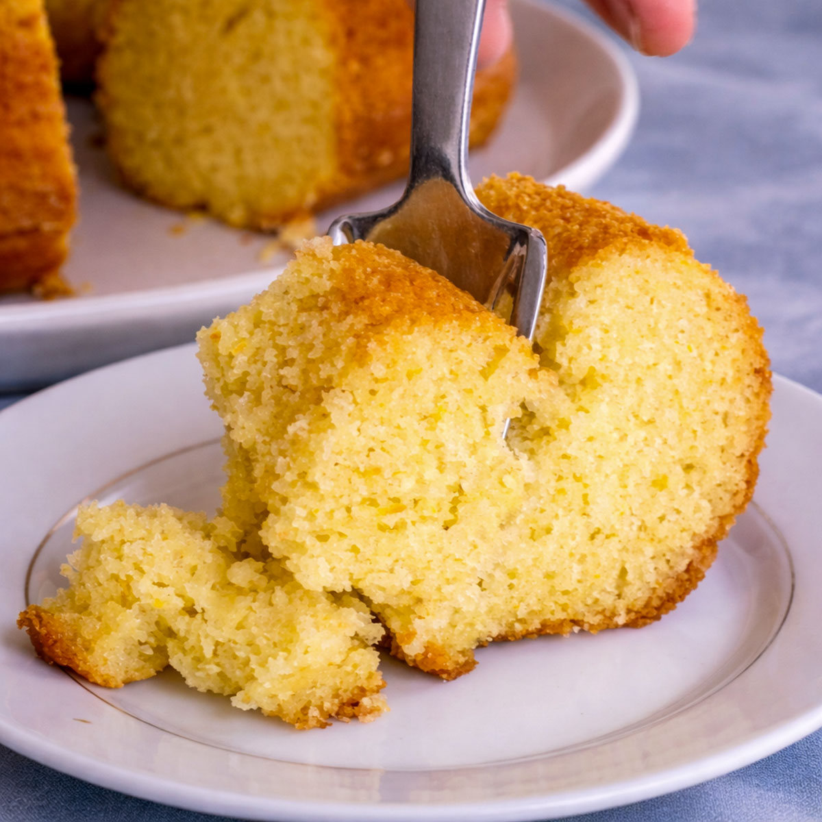 slice of orange juice cake on a white plate with a fork showing the soft moist citrus crumb