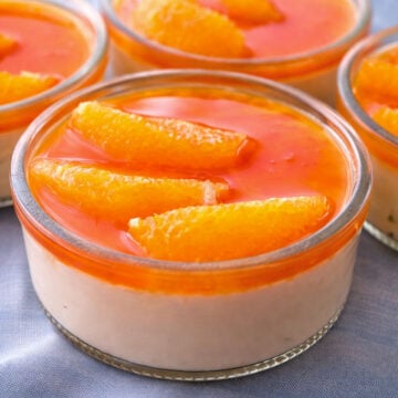Creamy orange custard in a glass ramekin, topped with glossy orange caramel and fresh orange segments, served as a bright citrus dessert.