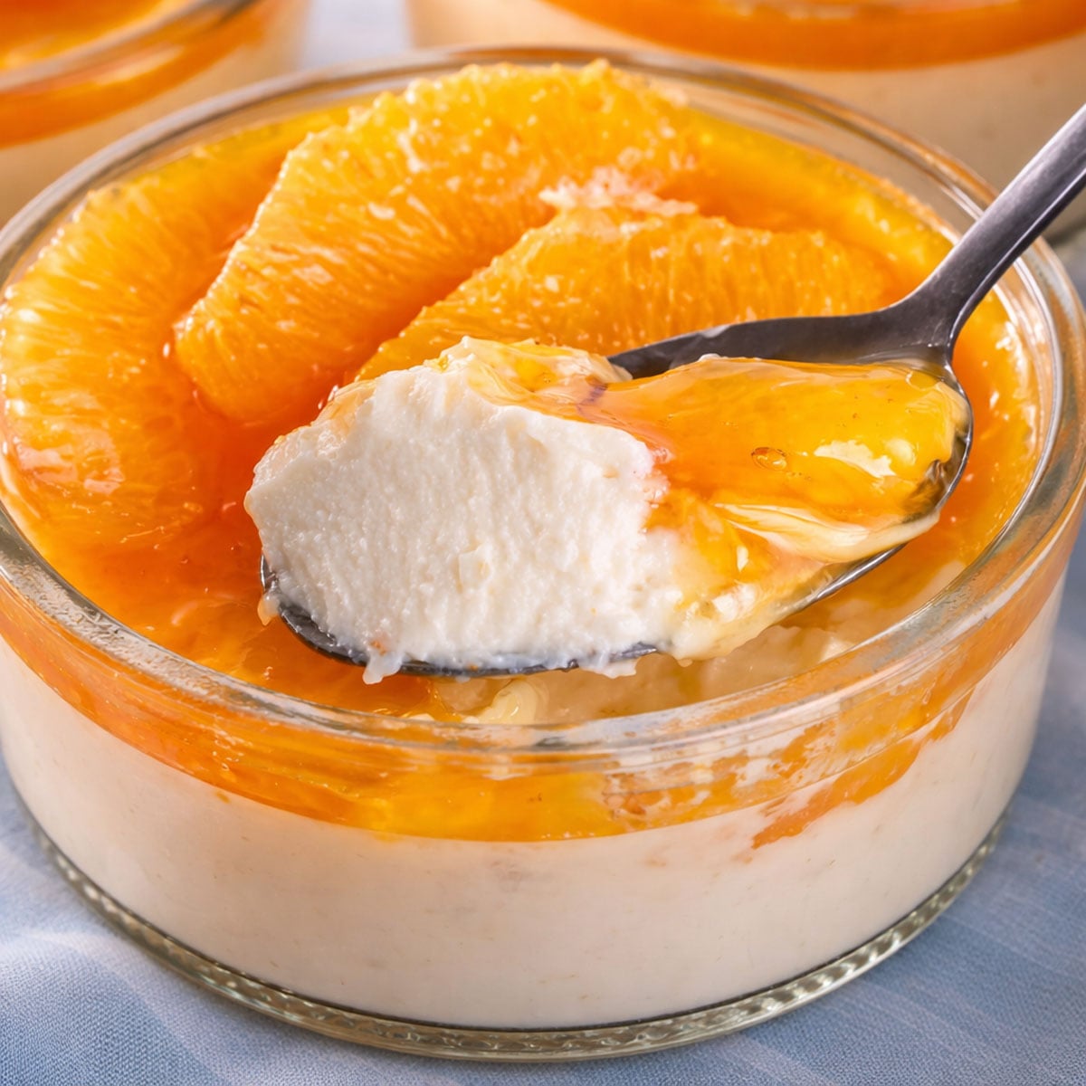 Spoonful of creamy orange custard lifted from a glass ramekin, topped with glossy orange segments and citrus caramel. 