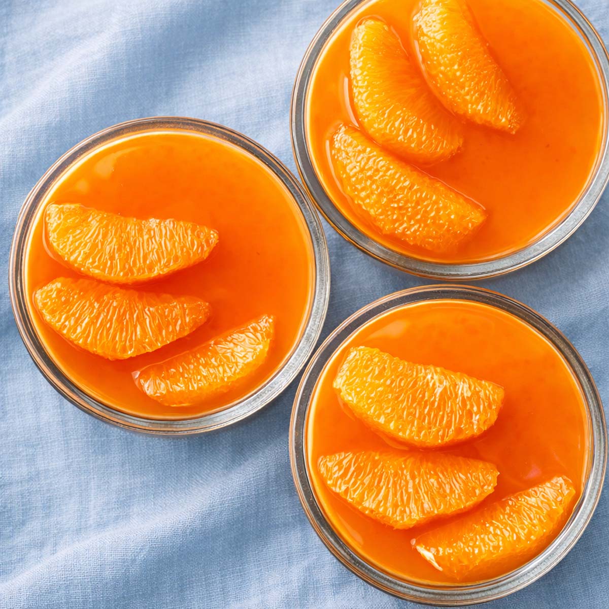 Overhead view of creamy orange custard in glass cups, topped with fresh orange segments, a bright citrus dessert. 