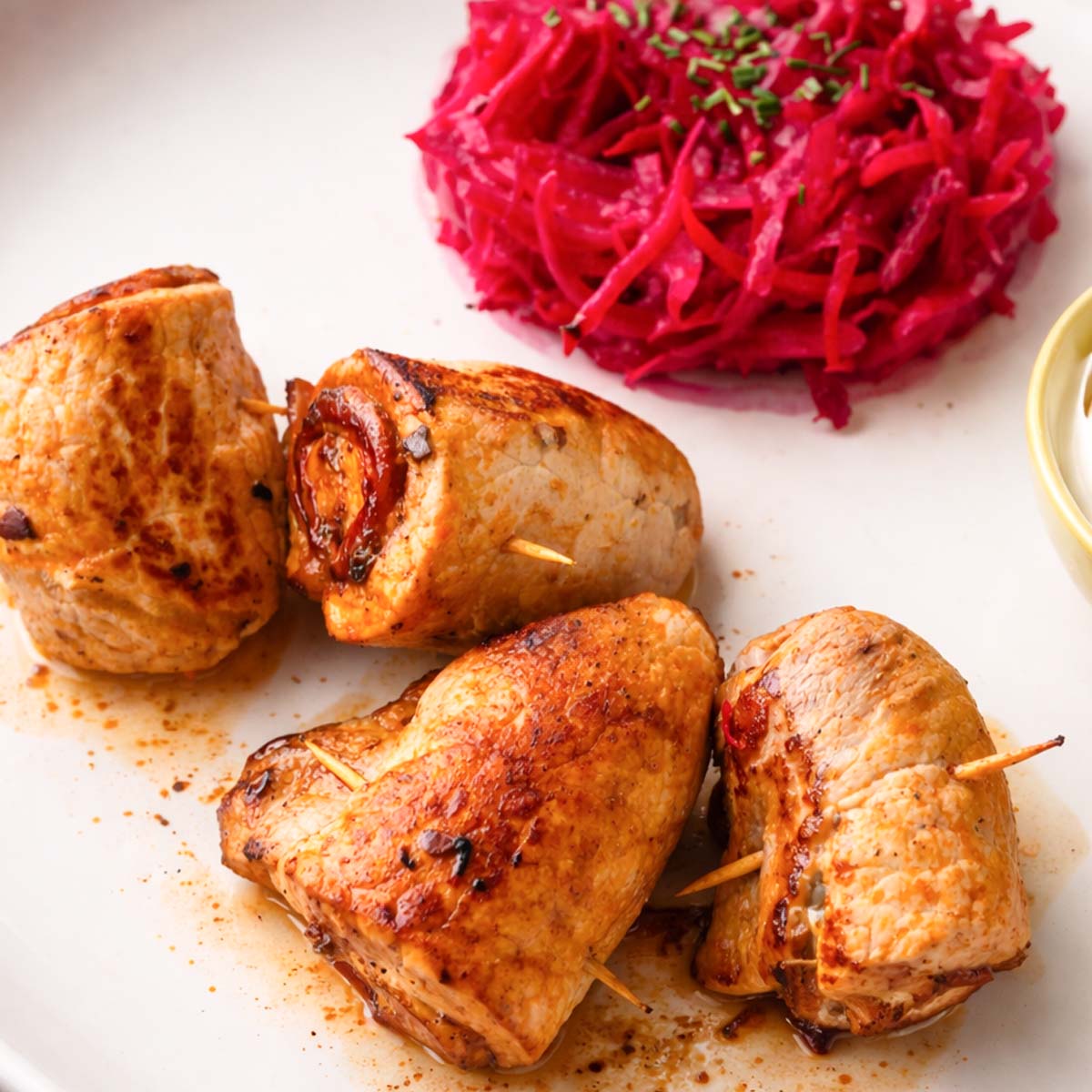 Stuffed pork rolls pan-seared until golden brown, served on a white plate with bright beet salad and sauce.