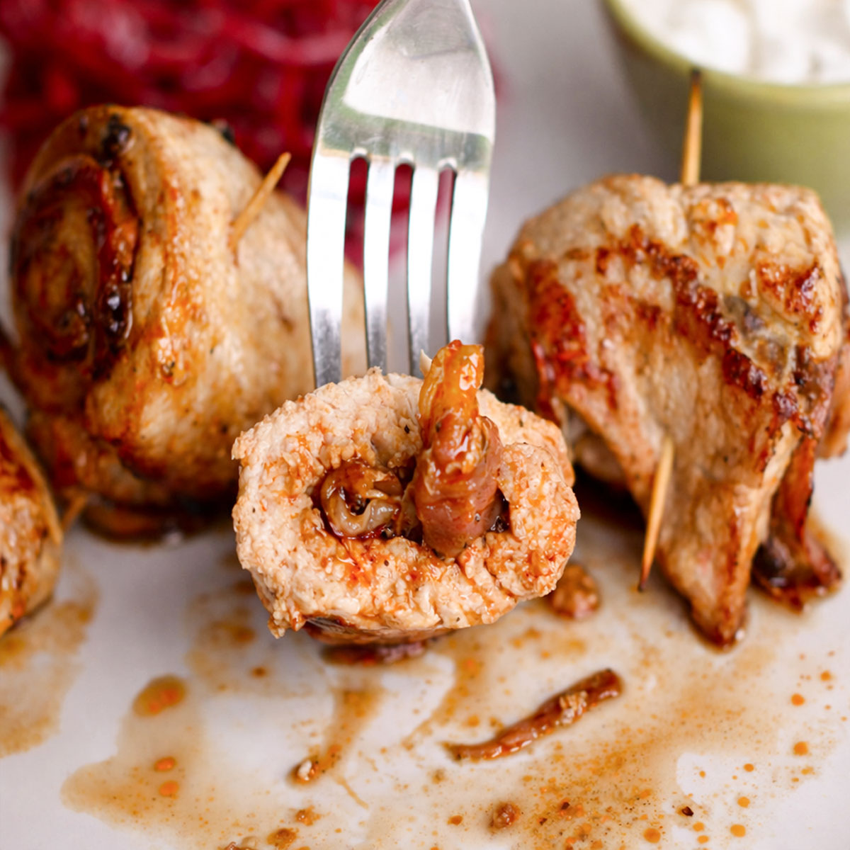 Fork lifting a sliced stuffed pork roll showing the savory filling, with golden seared pork rolls on a plate.