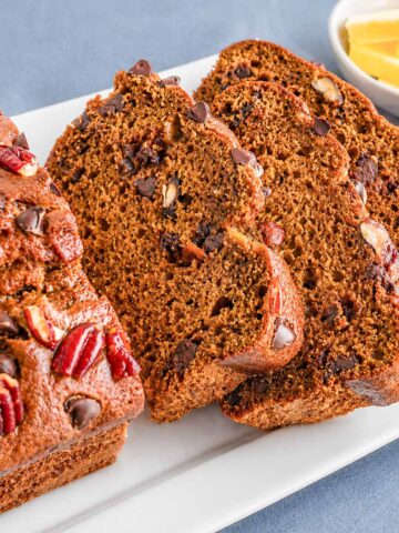 Pumpkin Bread with Chocolate Chips and Pecans sliced on a white plate, showing a moist crumb and topped with chocolate chips and pecan pieces