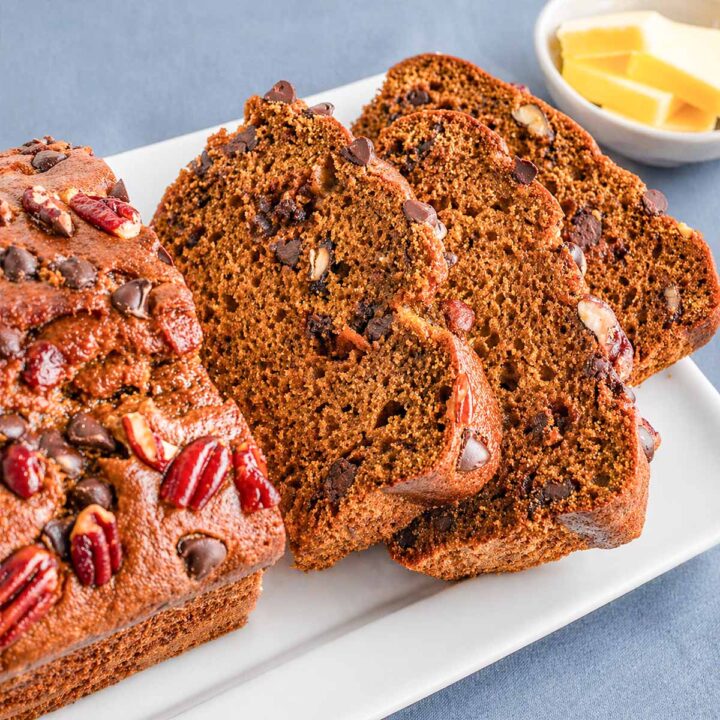Pumpkin Bread with Chocolate Chips and Pecans sliced on a white plate, showing a moist crumb and topped with chocolate chips and pecan pieces