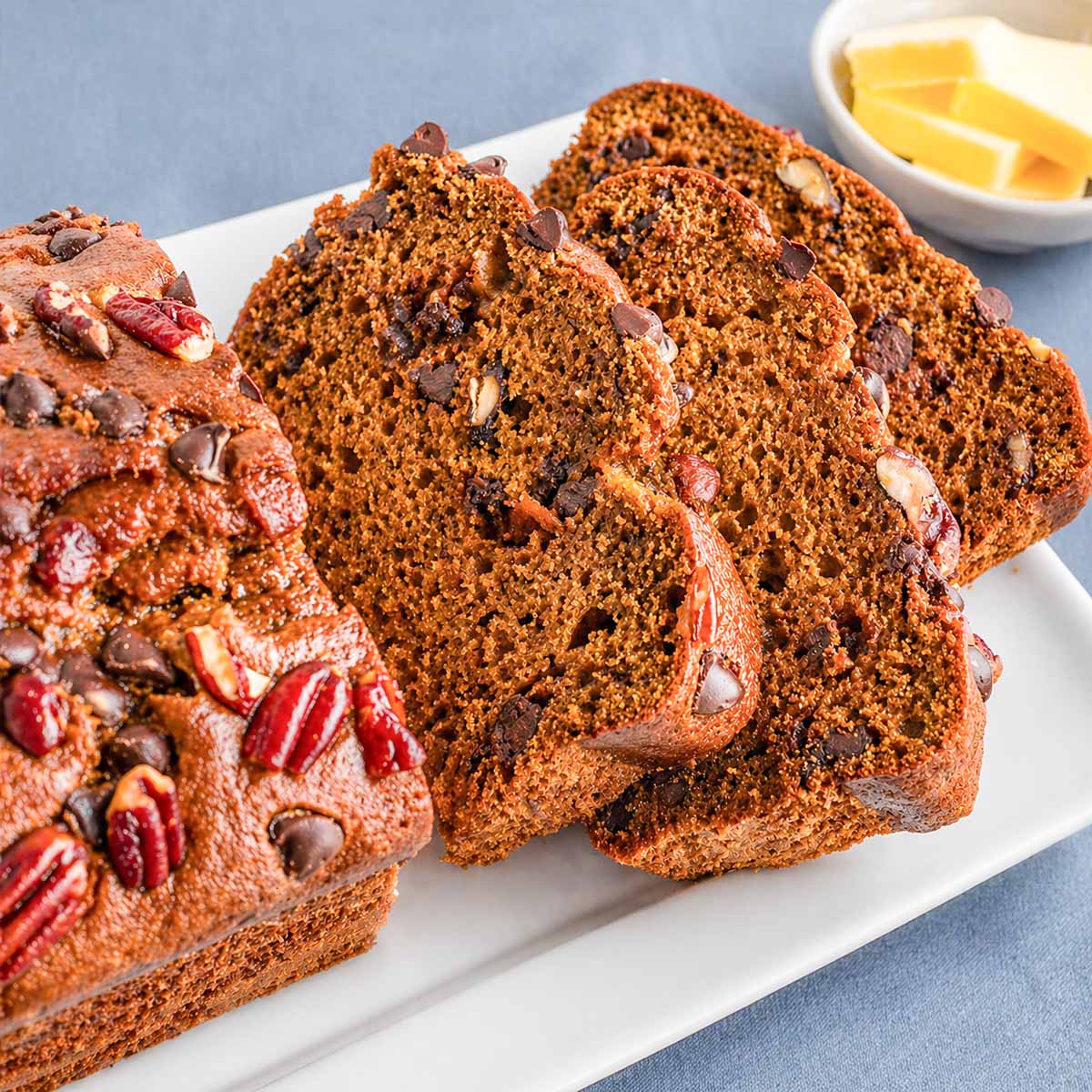 Pumpkin Bread with Chocolate Chips and Pecans sliced on a white plate, showing a moist crumb and topped with chocolate chips and pecan pieces