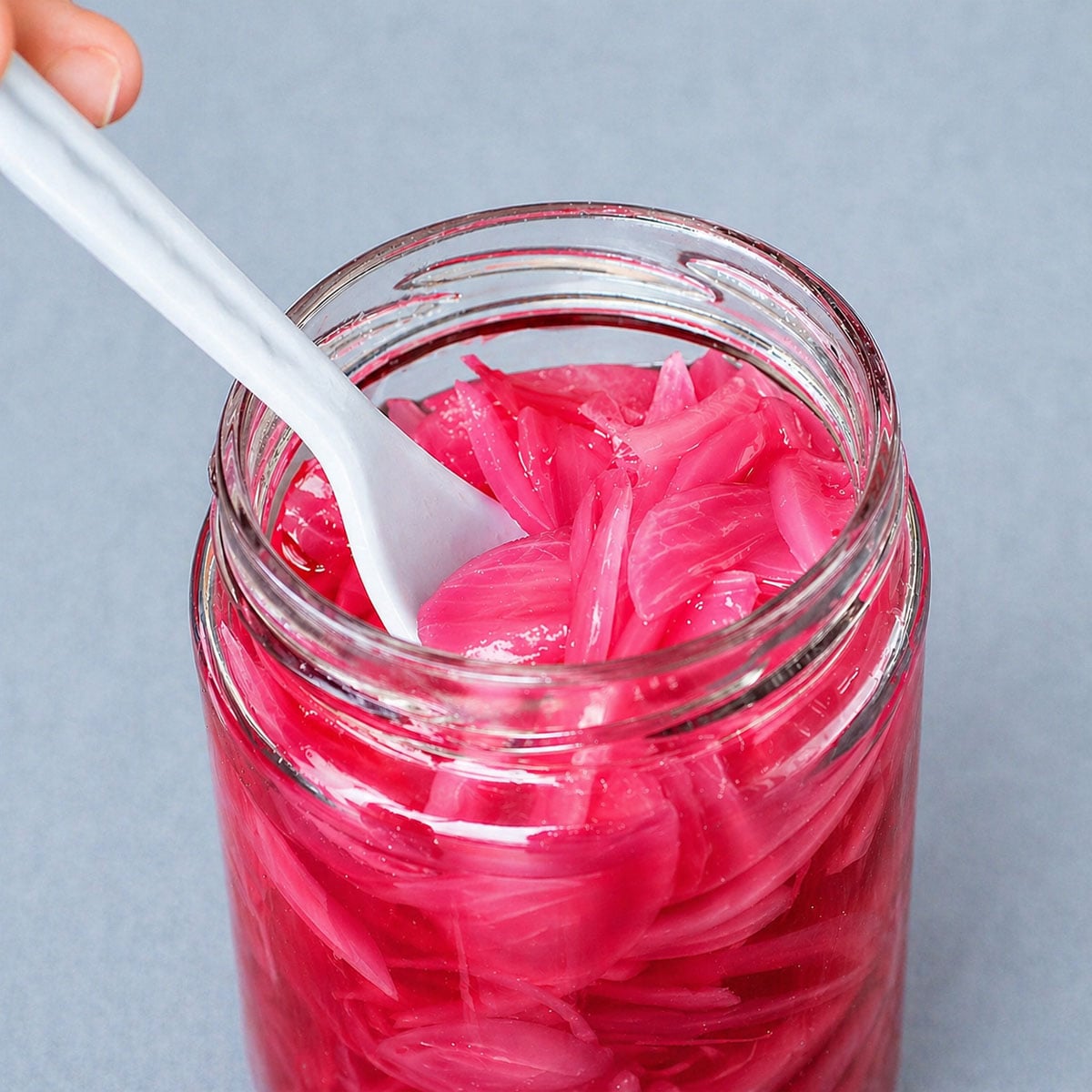 Quick pickled red onions in glass jar with white spoon