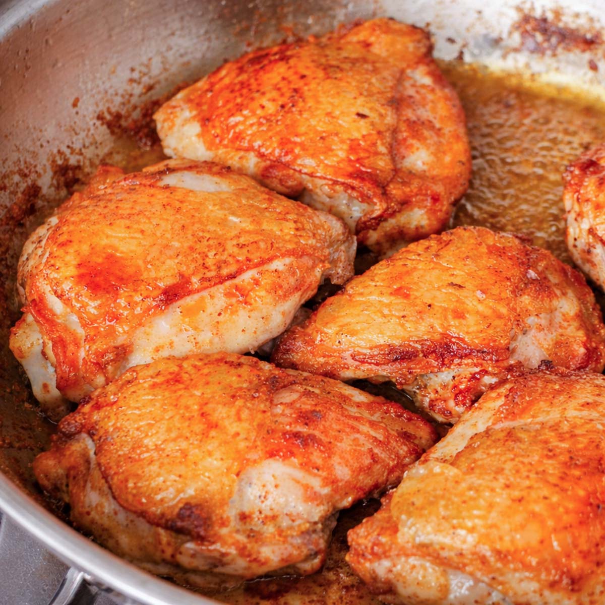 Crispy skillet chicken thighs browning in a pan, showing golden seared chicken with crisp skin during cooking.
