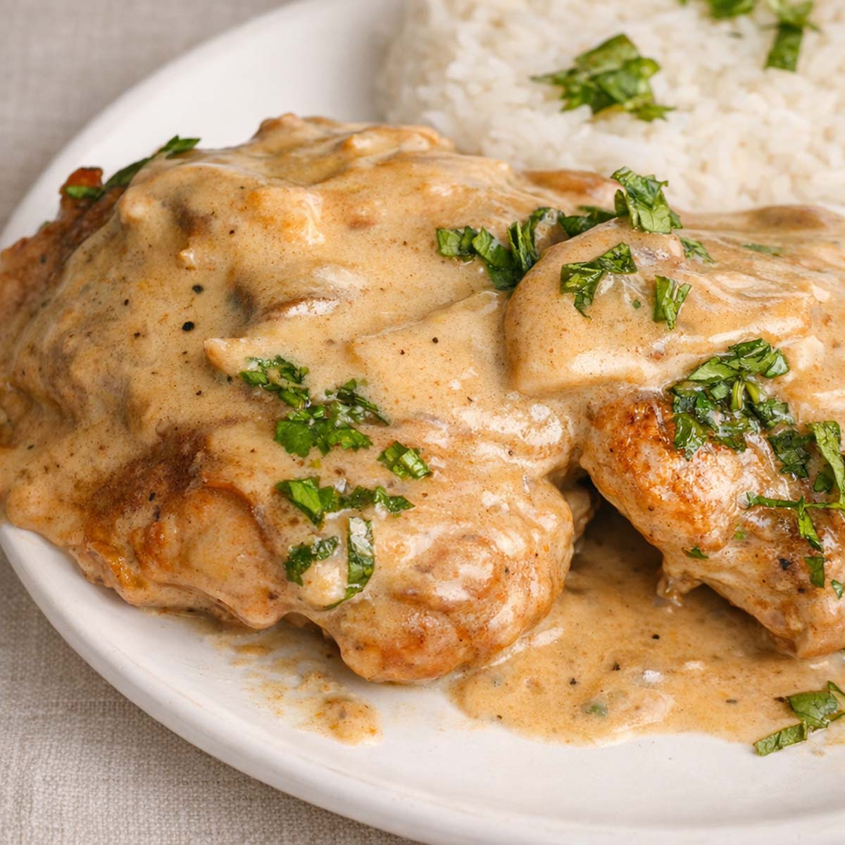 Creamy skillet chicken thighs served with rice, topped with mushroom sauce and fresh herbs on a plate.