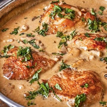 Skillet chicken thighs simmering in a creamy mushroom sauce with fresh herbs in a pan.