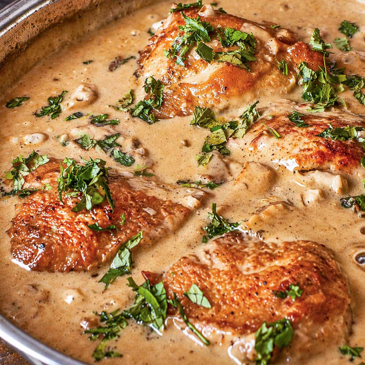 Skillet chicken thighs simmering in a creamy mushroom sauce with fresh herbs in a pan.